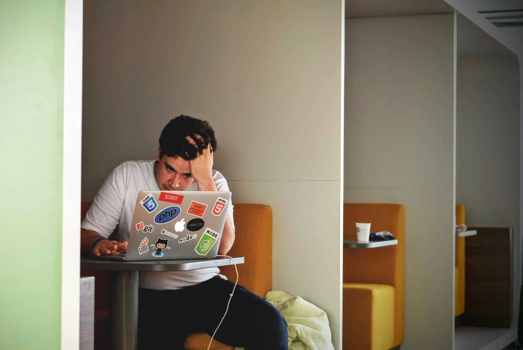 Ein junger Mann sitzt verwirrt an seinem Laptop